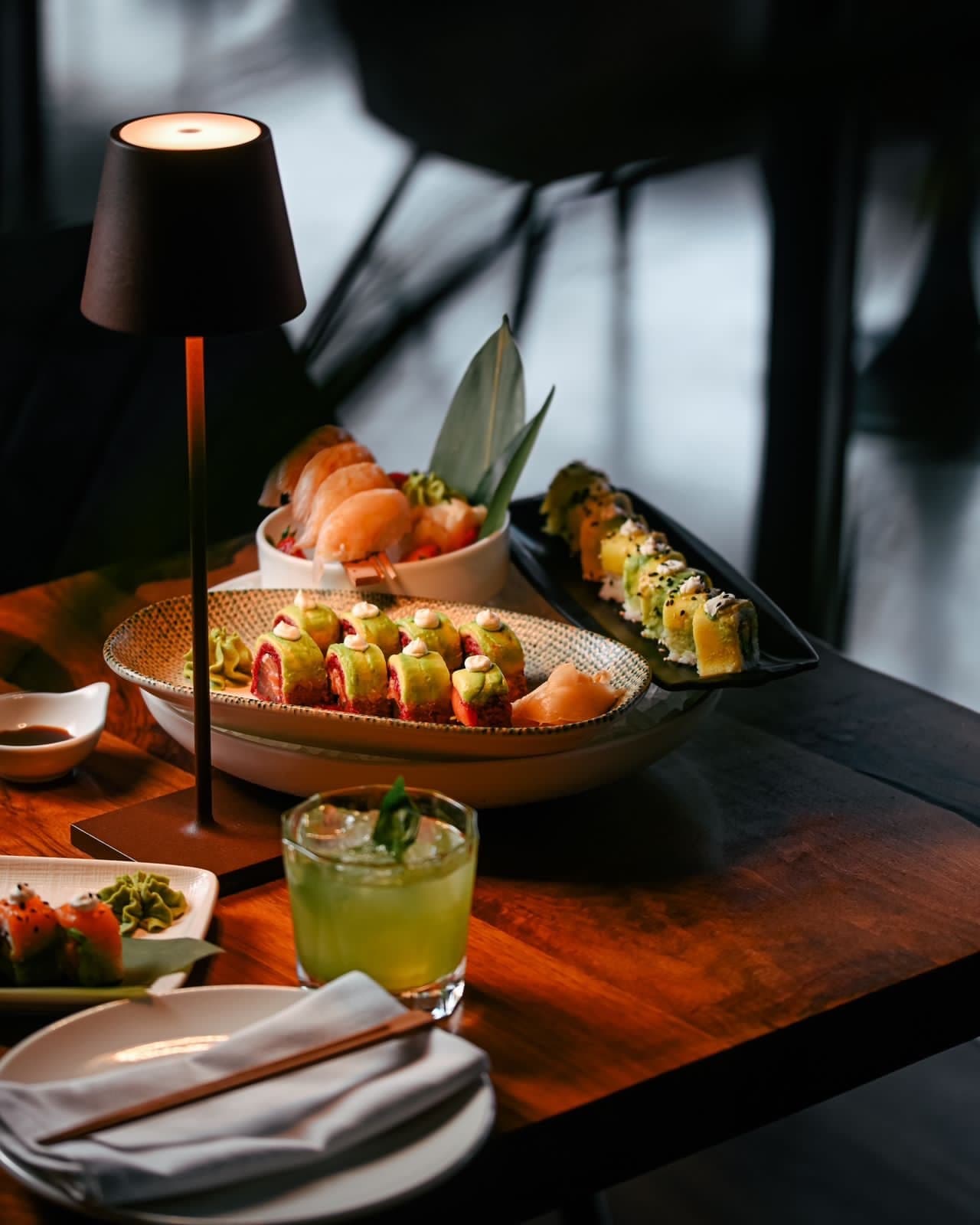A cocktail and sushi plate on the table under warm lamp light