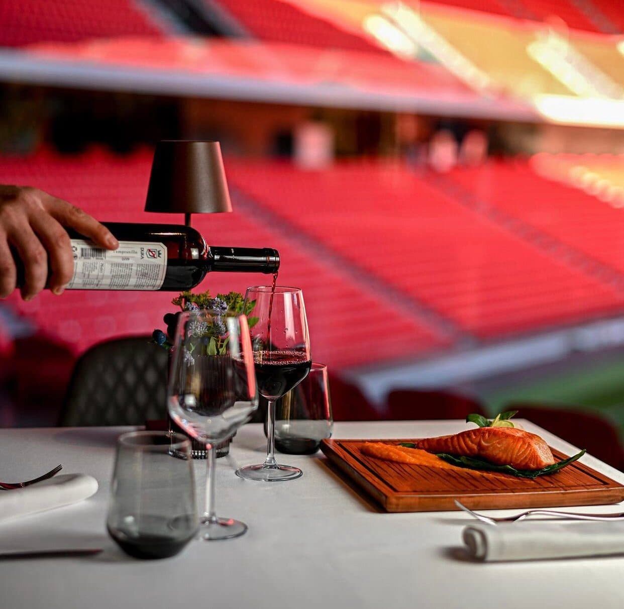 Wine poured tableside beside a plated salmon dish, the red stadium seats blurred behind