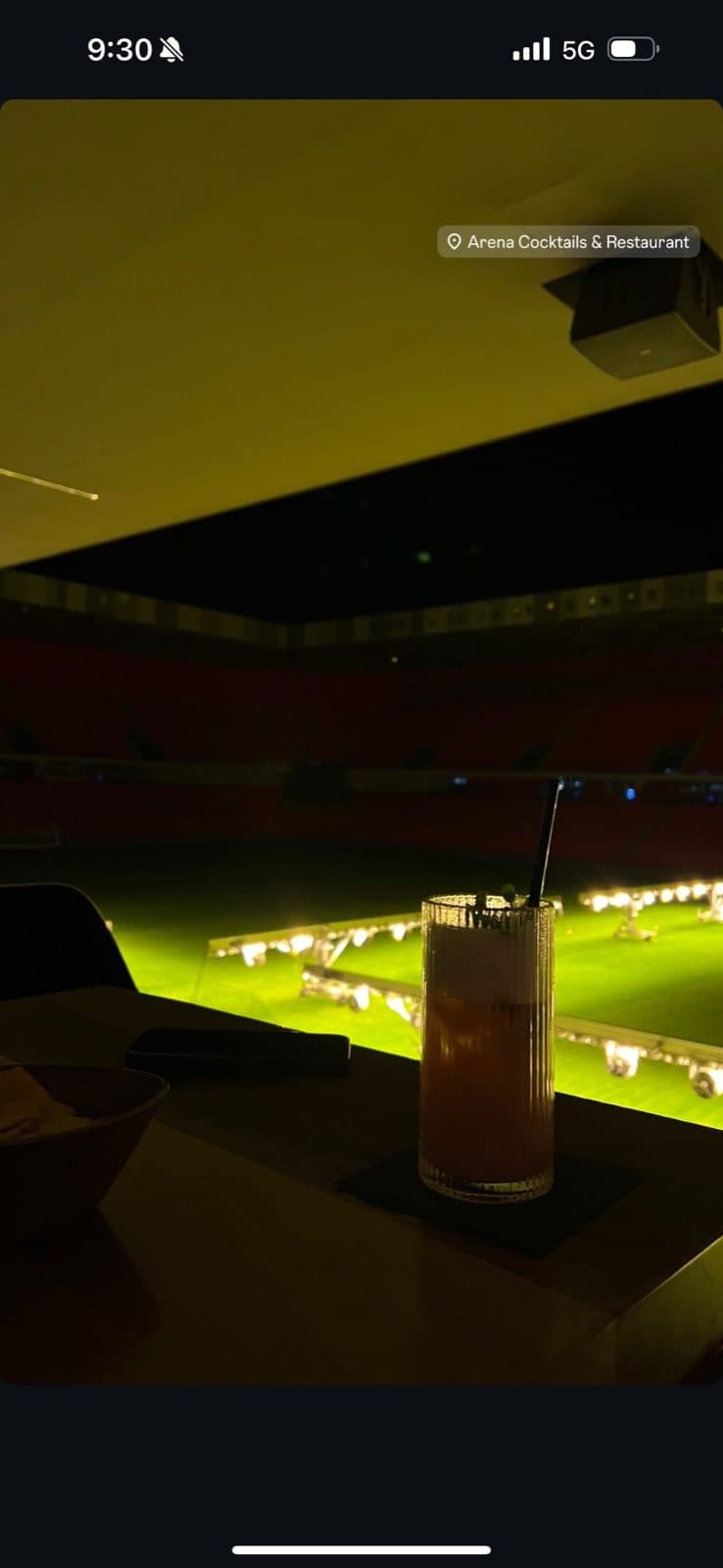Guest photo of a cocktail on the table at night with the floodlit pitch behind
