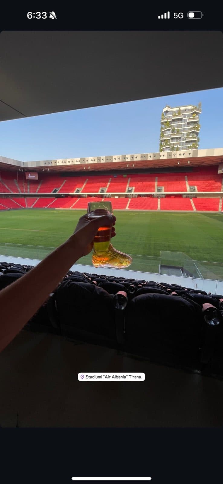 Guest photo holding up a beer with the pitch behind