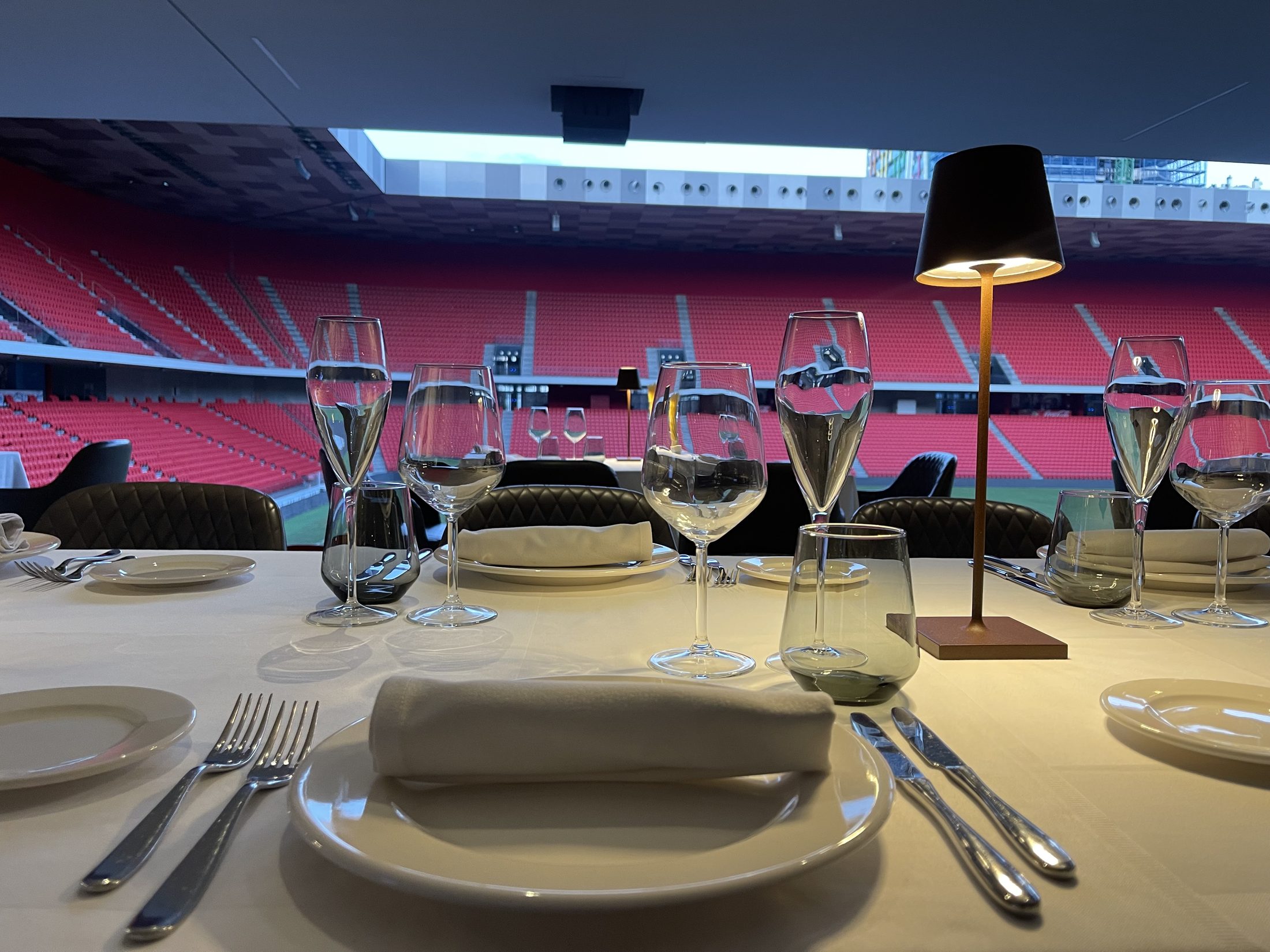 A set table with wine glasses against the floor-to-ceiling glass overlooking the stadium seats