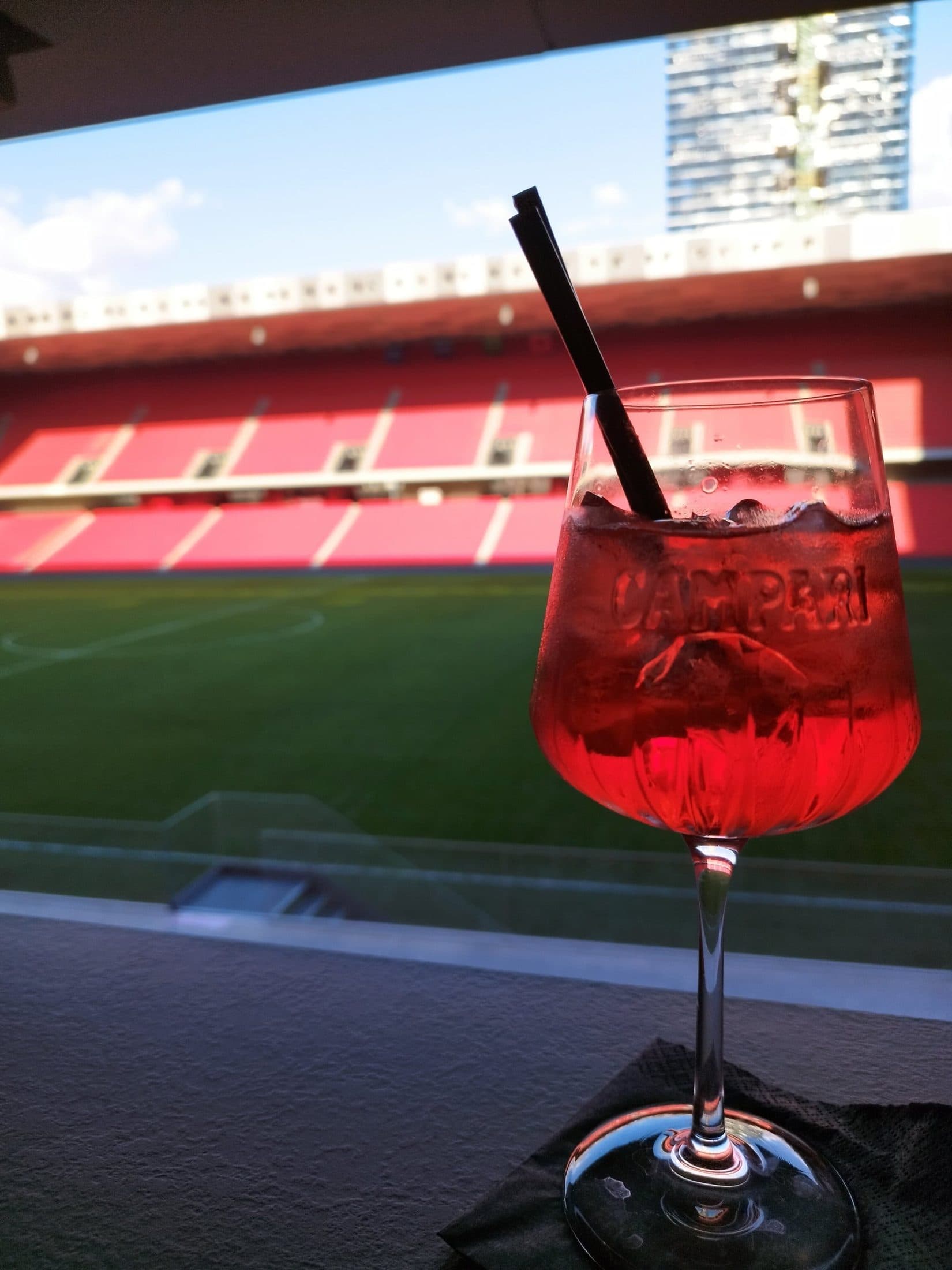 A Campari spritz on the table with the stadium seats and pitch visible through the glass wall