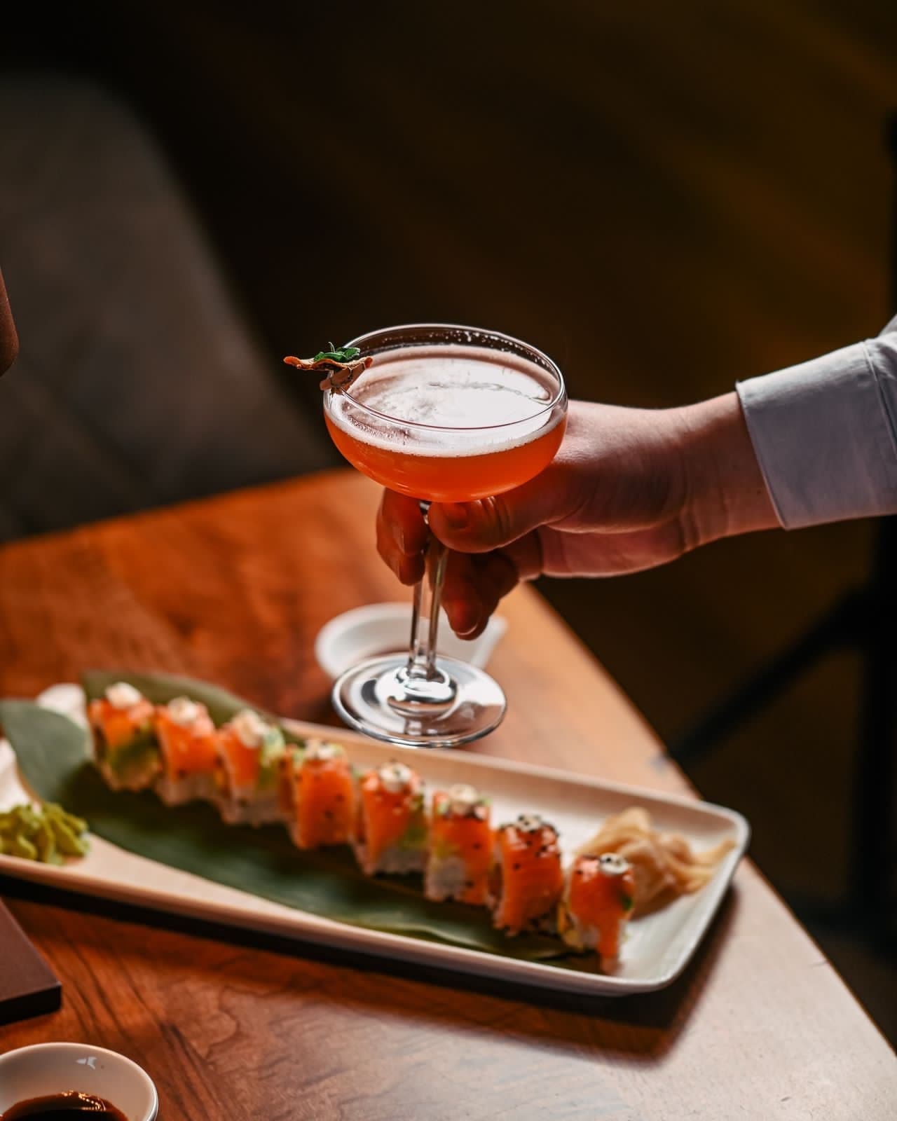 Staff holding up a coupe cocktail beside a sushi plate