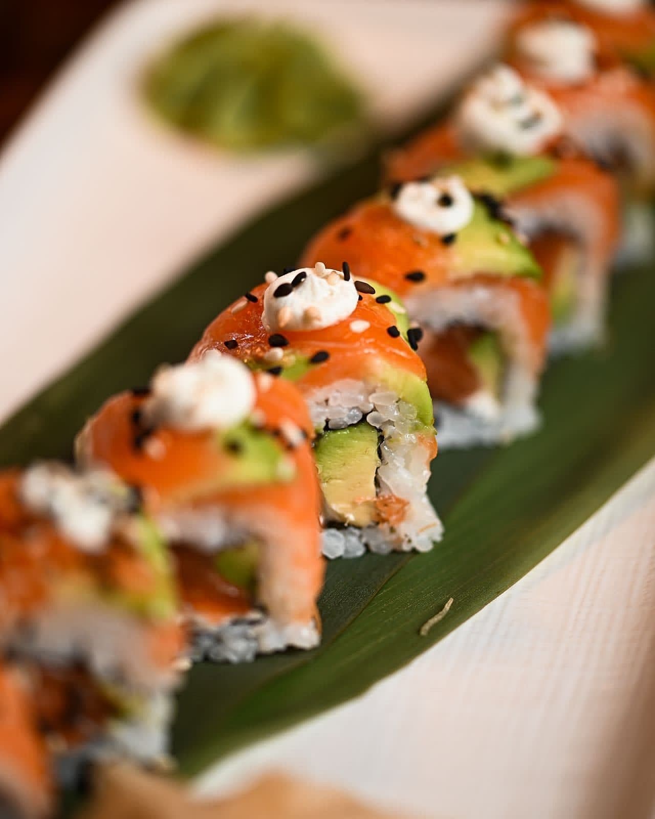 Salmon and avocado sushi rolls topped with a cream drizzle and sesame, served on a banana leaf