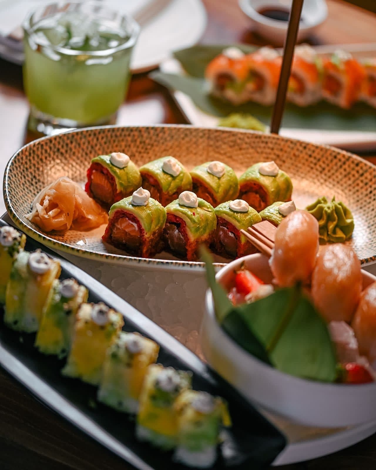 A sushi platter with pickled ginger and ponzu, a green cocktail glass visible at the edge of the table