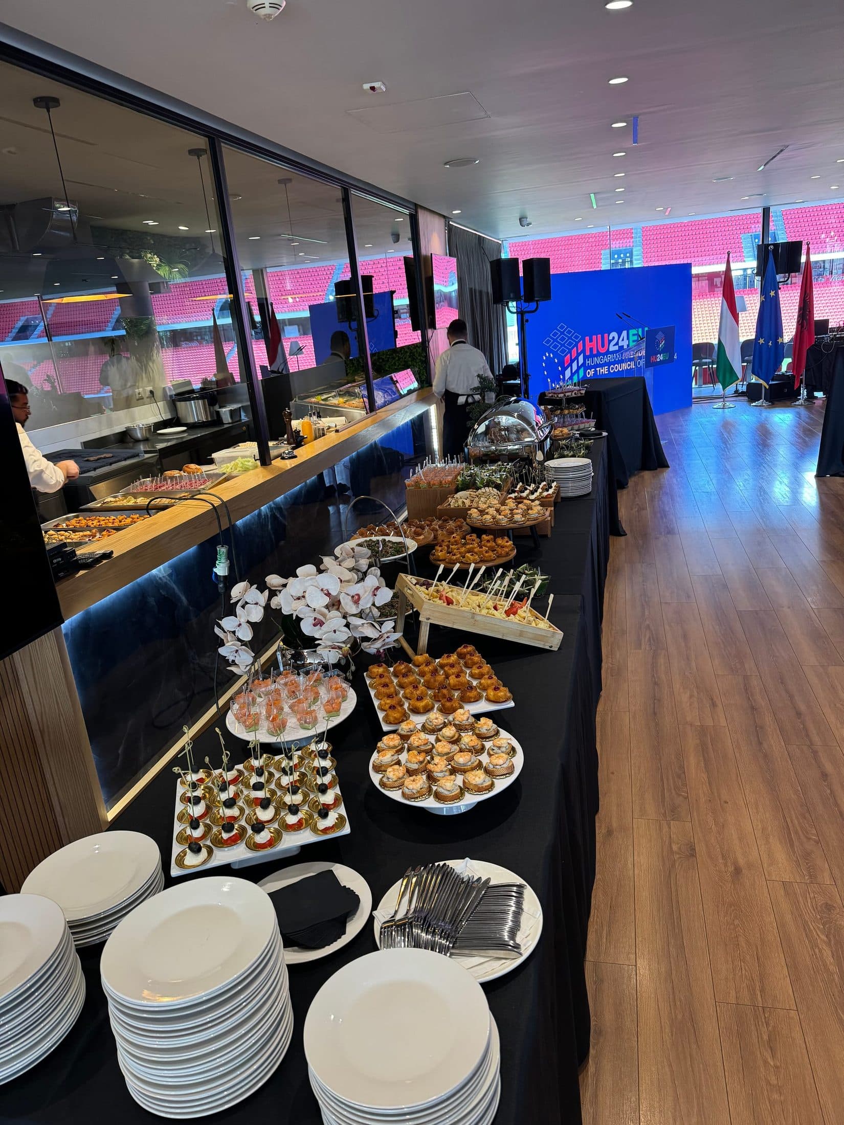Buffet counter beside the glass wall onto the stadium, branded backdrop and flags in the background
