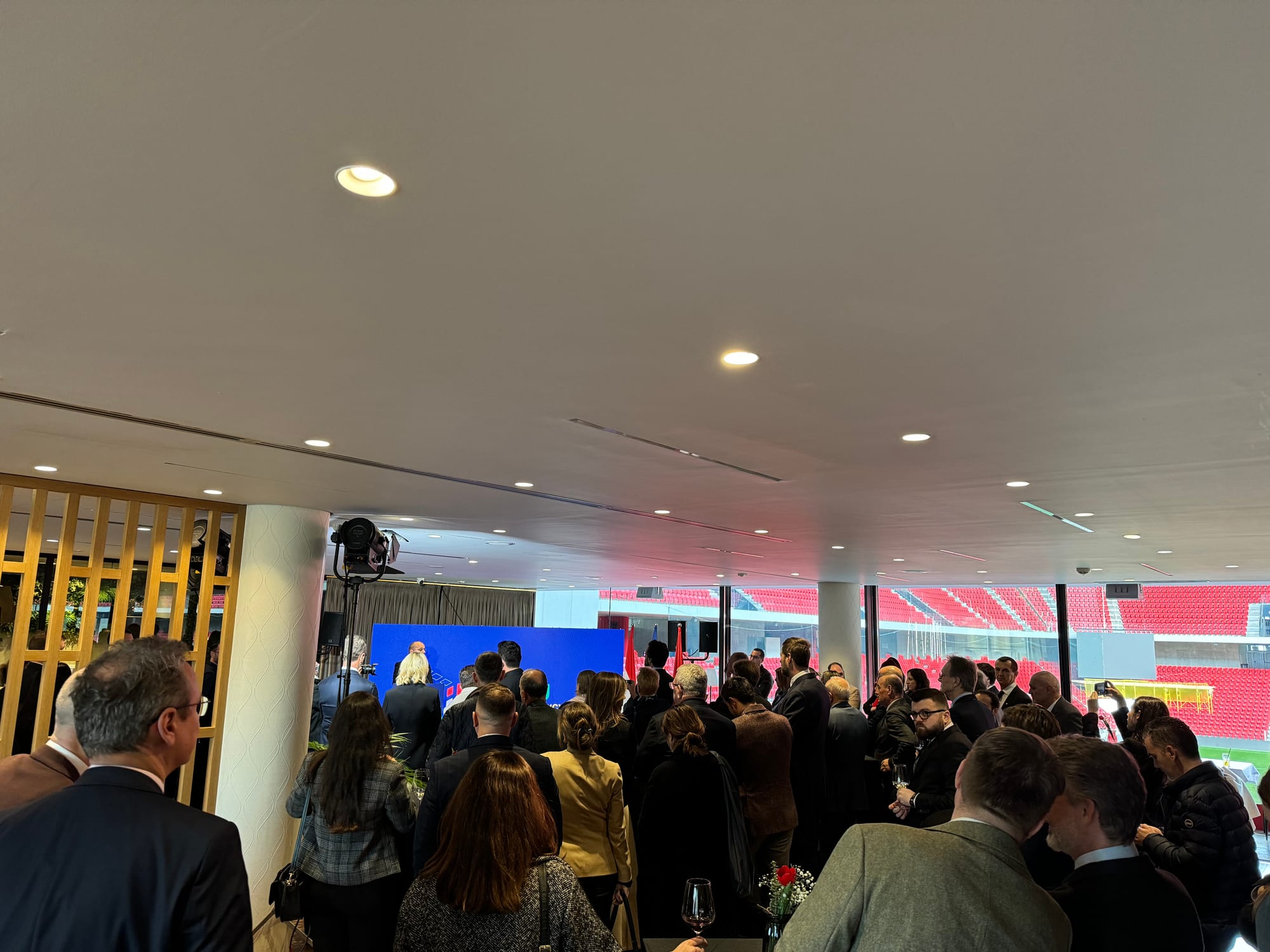 Branded stage backdrop with flags and a podium, stadium seating visible through the glass