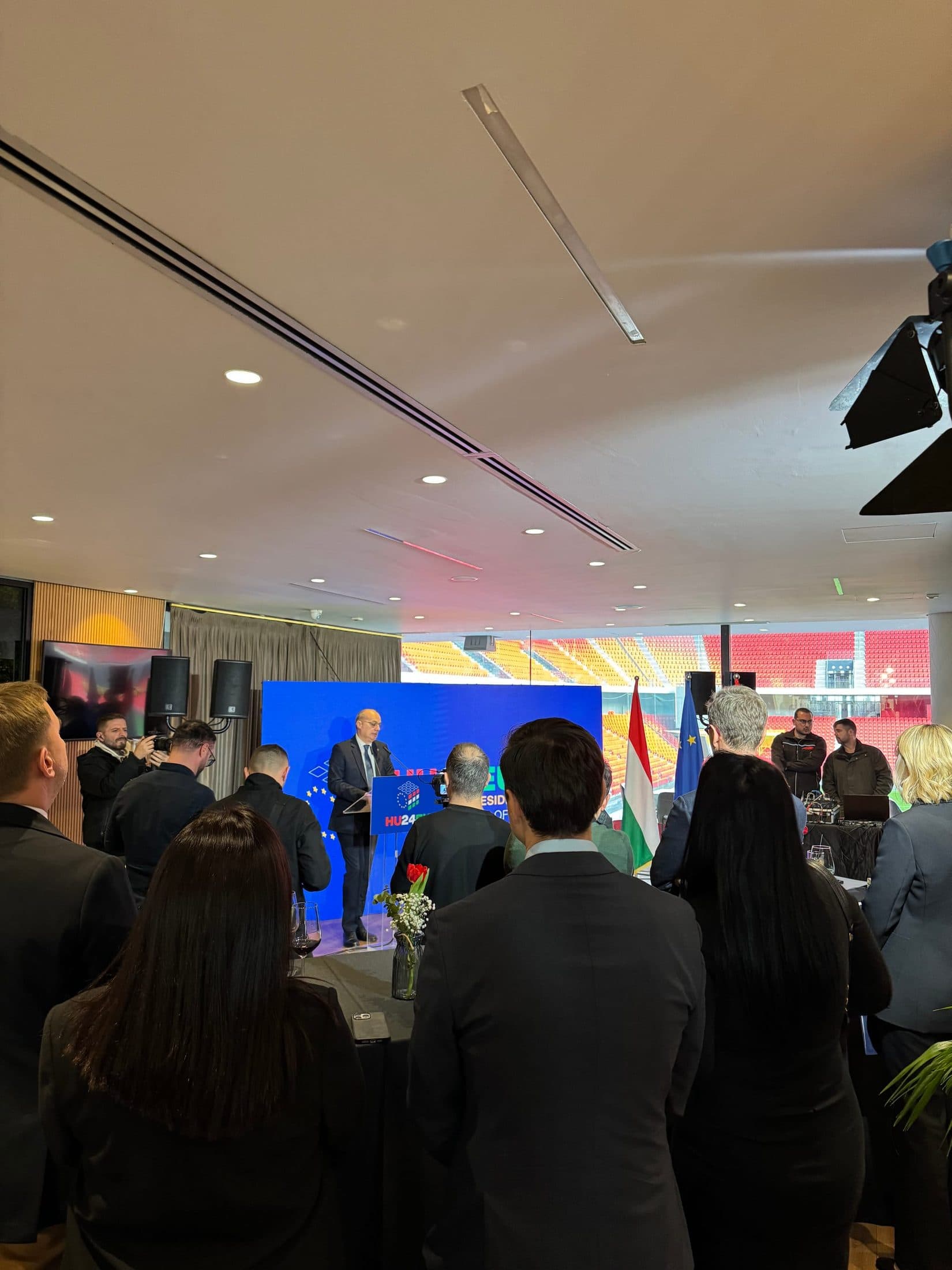 A speaker addressing guests from a branded podium, the stadium bowl visible behind