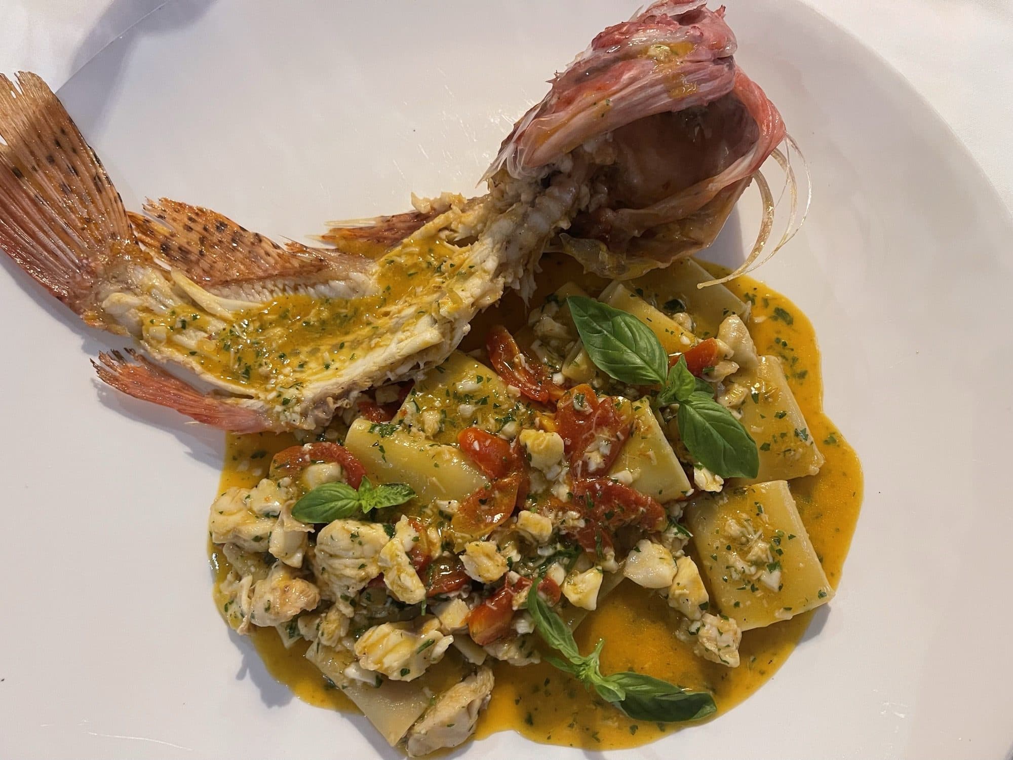 Crab ravioli plated alongside a whole grilled fish