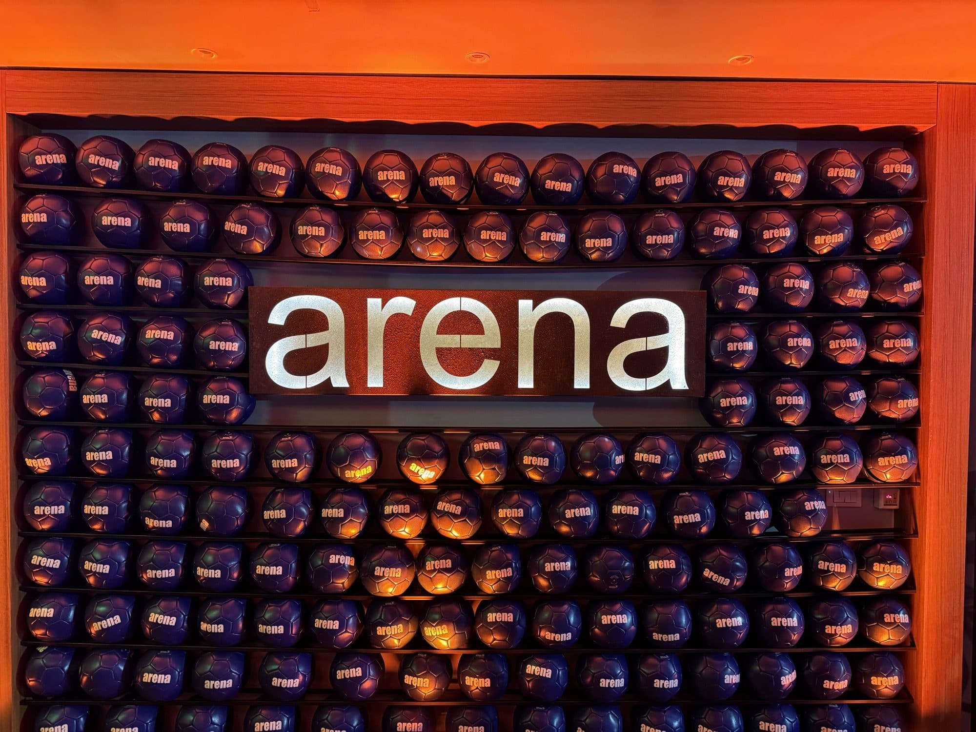 Backlit Arena wordmark set into a wall of branded footballs