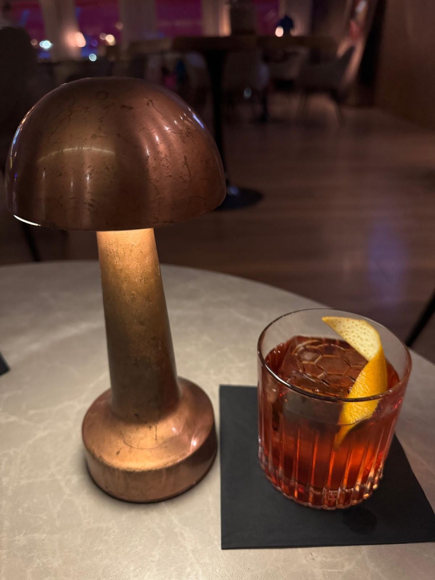 A Negroni beside a copper mushroom lamp on the bar table